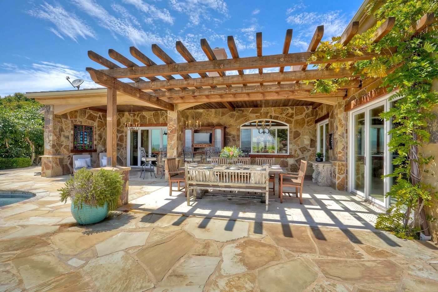 Covered stone pavilion with pergola, chandelier dining, and outdoor kitchen