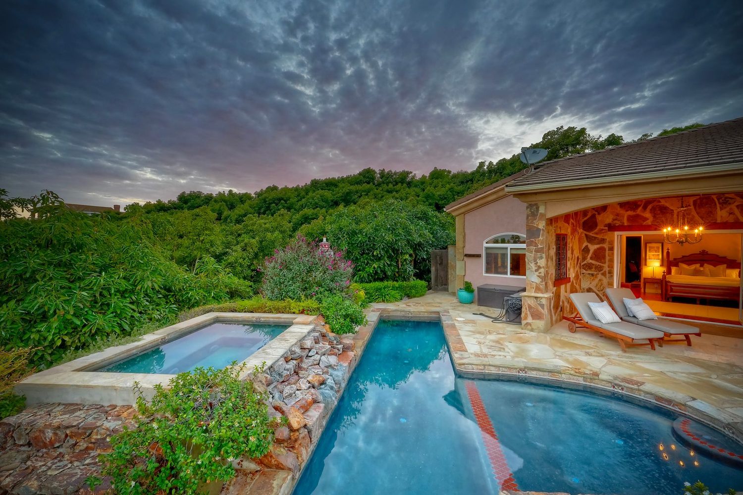 Lap pool and elevated spa at dusk beside the primary wing, framed by the avocado grove
