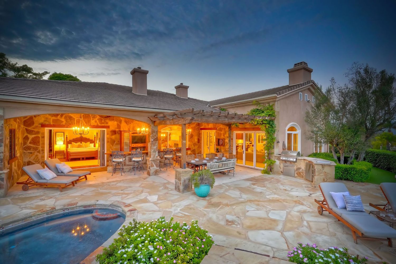 Covered stone pavilion and outdoor kitchen lit at twilight at 2484 Dos Lomas