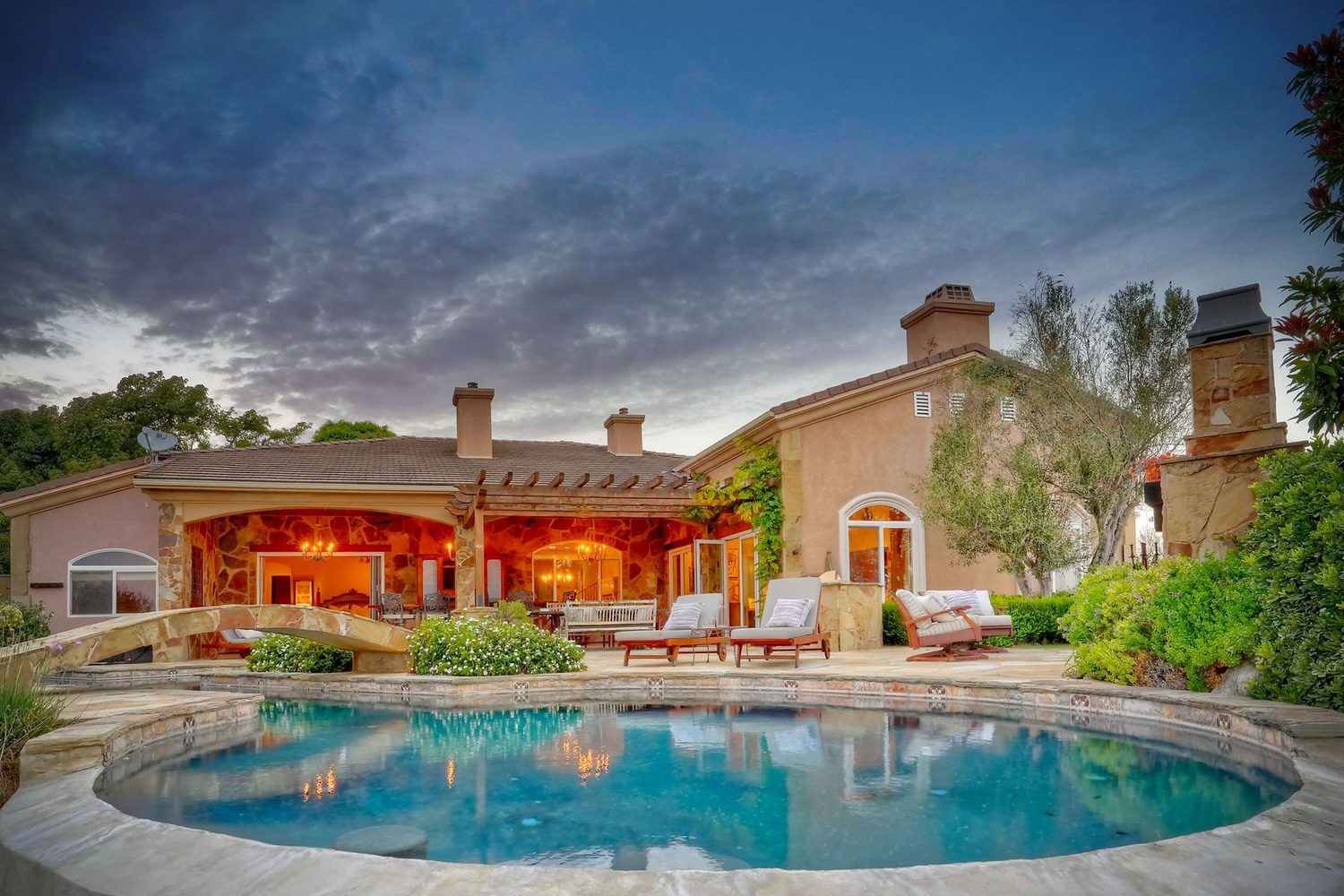 2484 Dos Lomas at twilight — stone loggia and pool glowing at dusk in Champagne Crest, Fallbrook